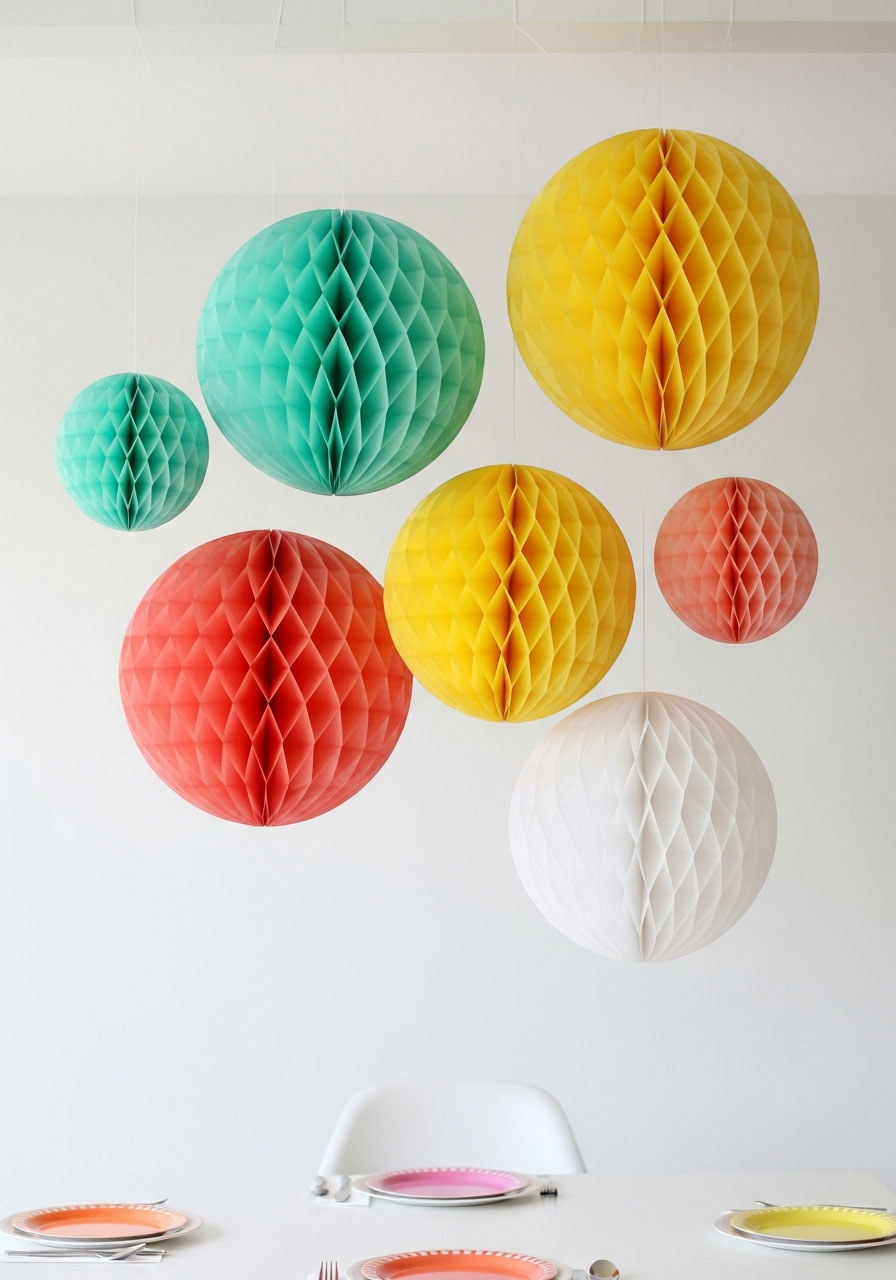 Colorful honeycomb pom pom balls in mint, coral and yellow hanging above table - modern DIY birthday party decoration