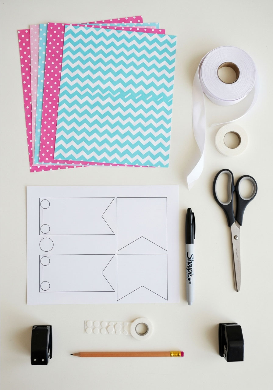 Flatlay of DIY birthday banner supplies including scrapbook paper, scissors, ribbon, markers and template