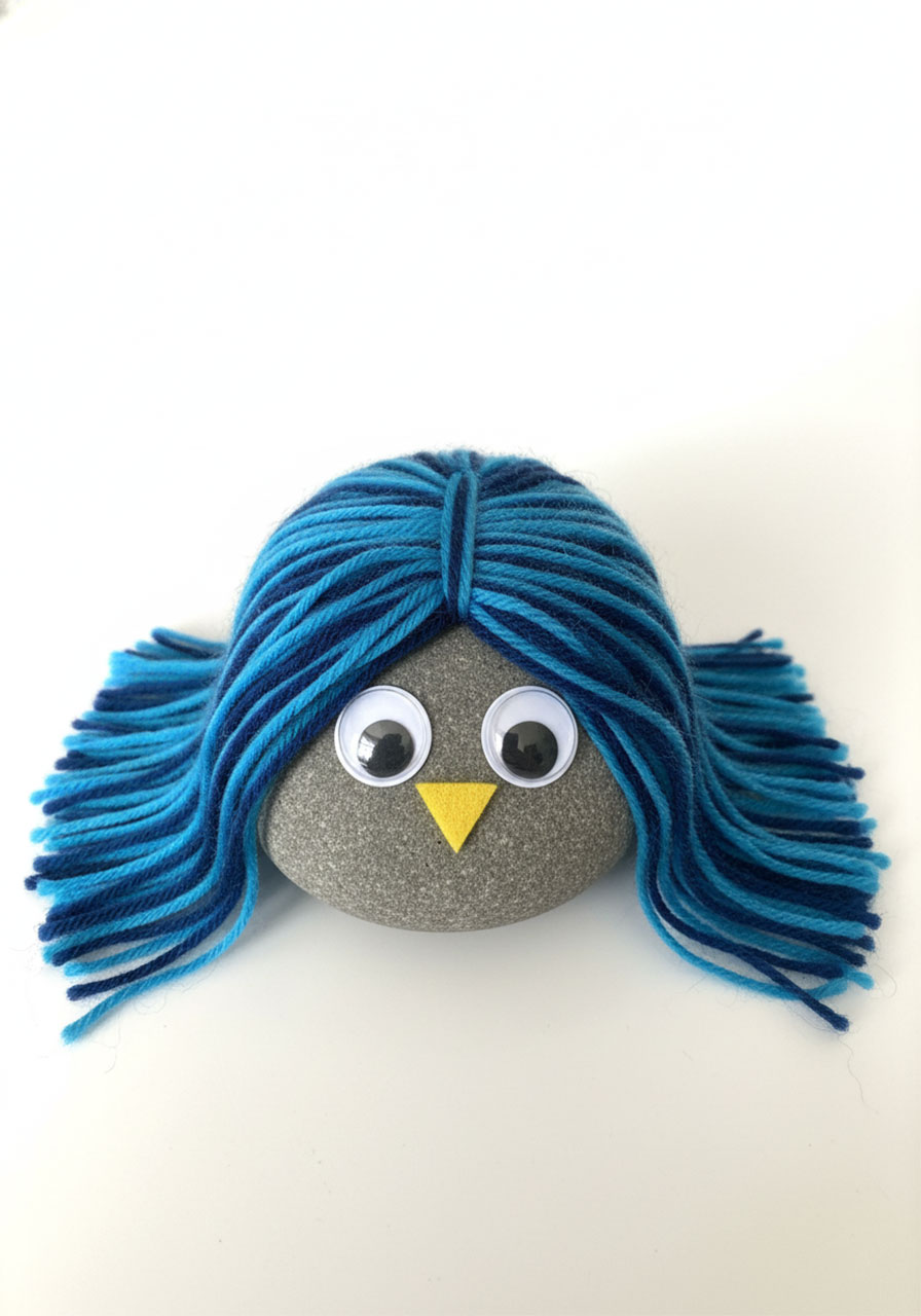 Long-haired fluffy pet rock variation showing blue yarn pieces arranged horizontally and vertically for flowing hair effect