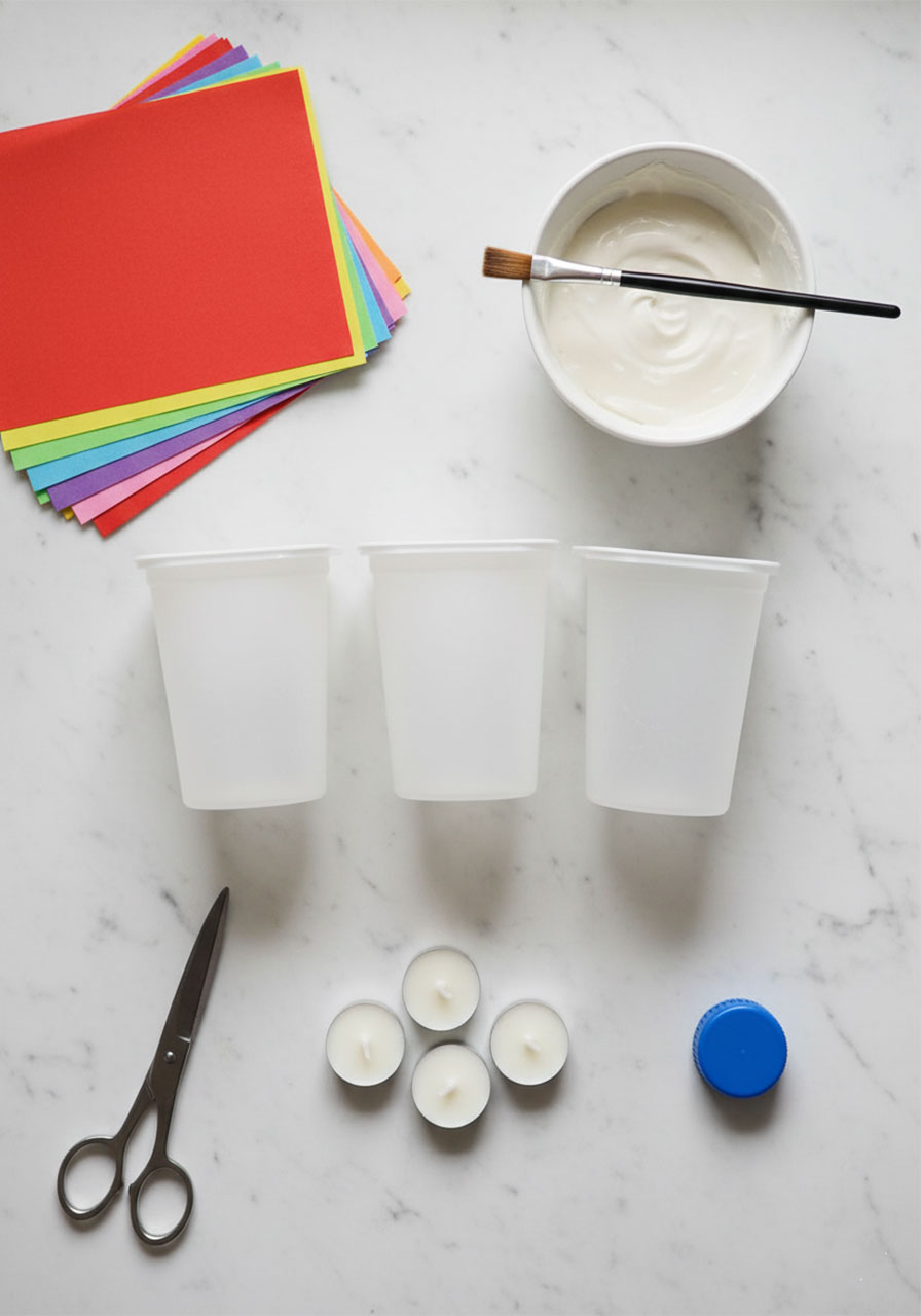 Flat lay of craft supplies needed for tissue paper lanterns including yogurt containers, colorful tissue paper, mod podge, scissors and LED candles