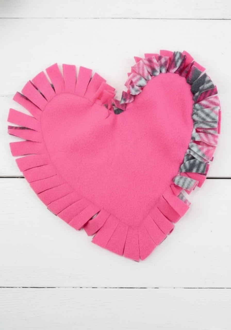 Child's hands tying first knot with fleece strips on no-sew heart pillow craft project