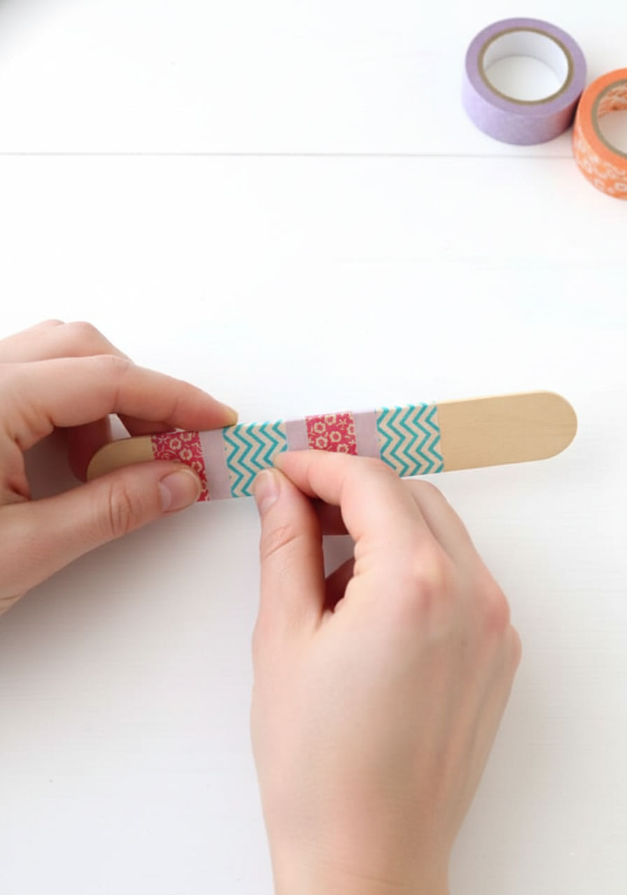 Scissors cutting jumbo craft stick to size for mini banjo handle with measurement marks visible
