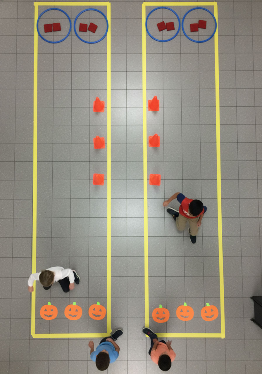 Overhead view of hallway obstacle course with two lanes showing children racing through stepping stones cones and hula hoops - team party game for elementary kids