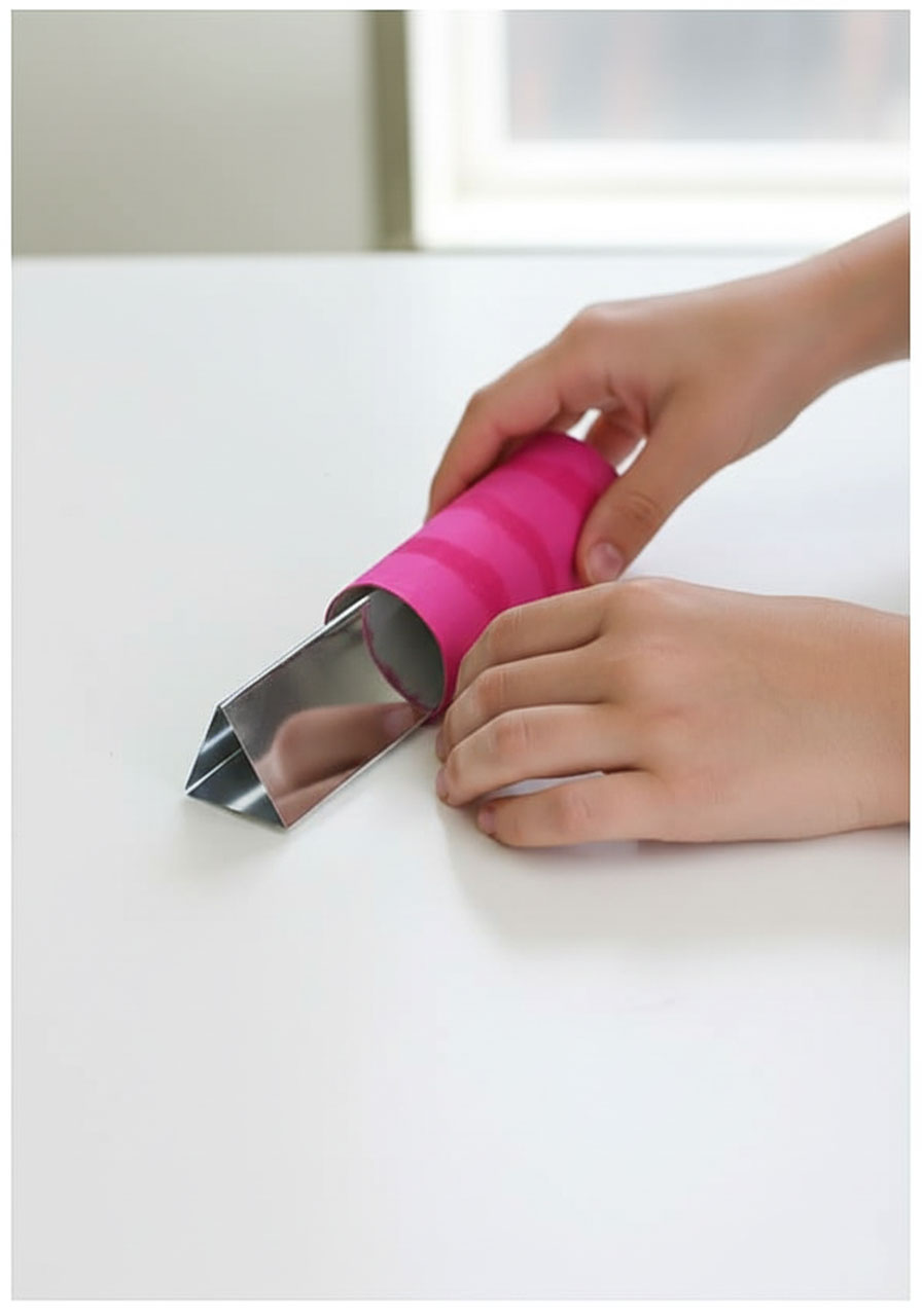 Child inserting reflective triangular prism into painted cardboard tube during kaleidoscope assembly