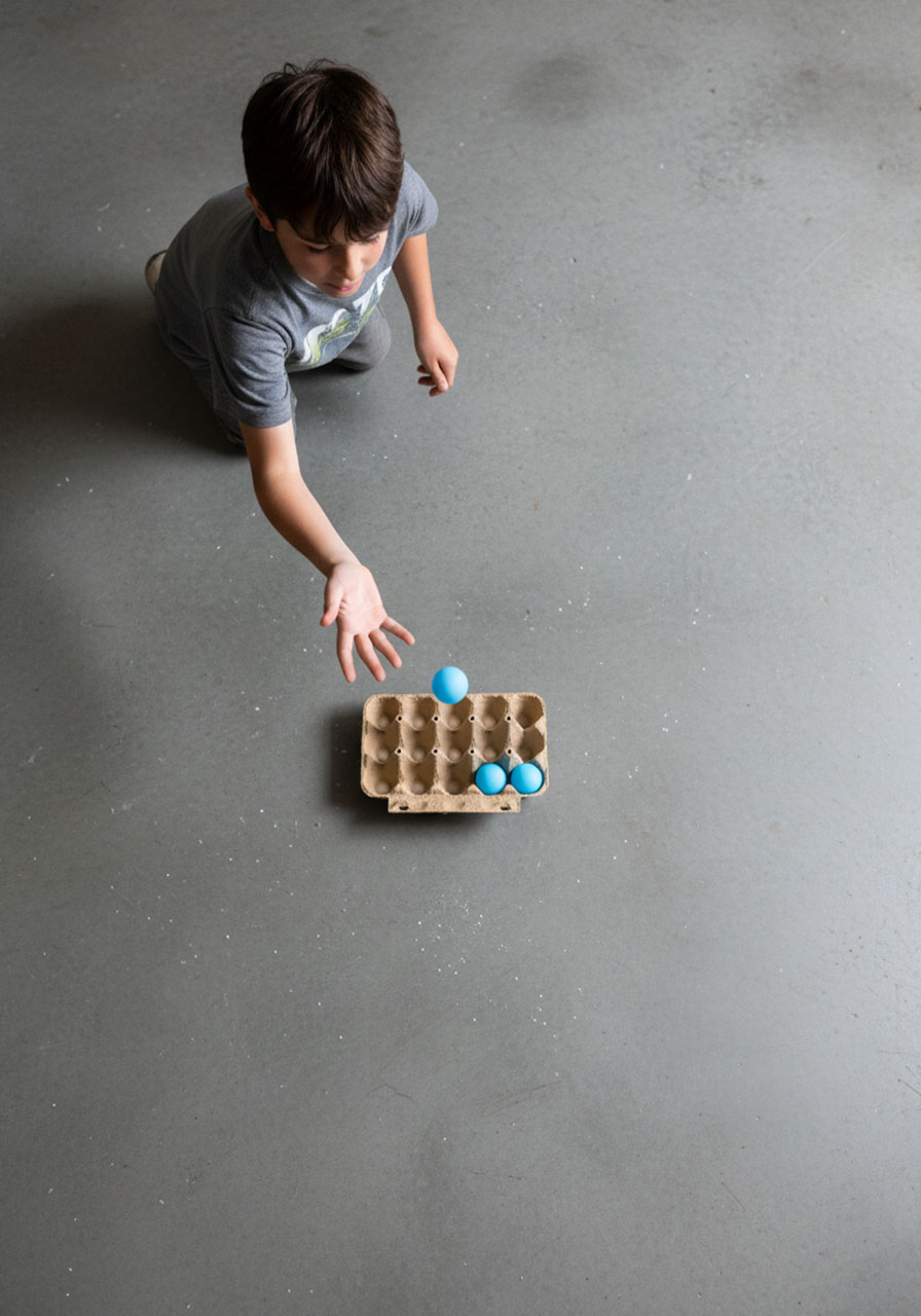 Overhead view of the Ponginator game setup, showing a boy bouncing a ping pong ball into an egg carton.