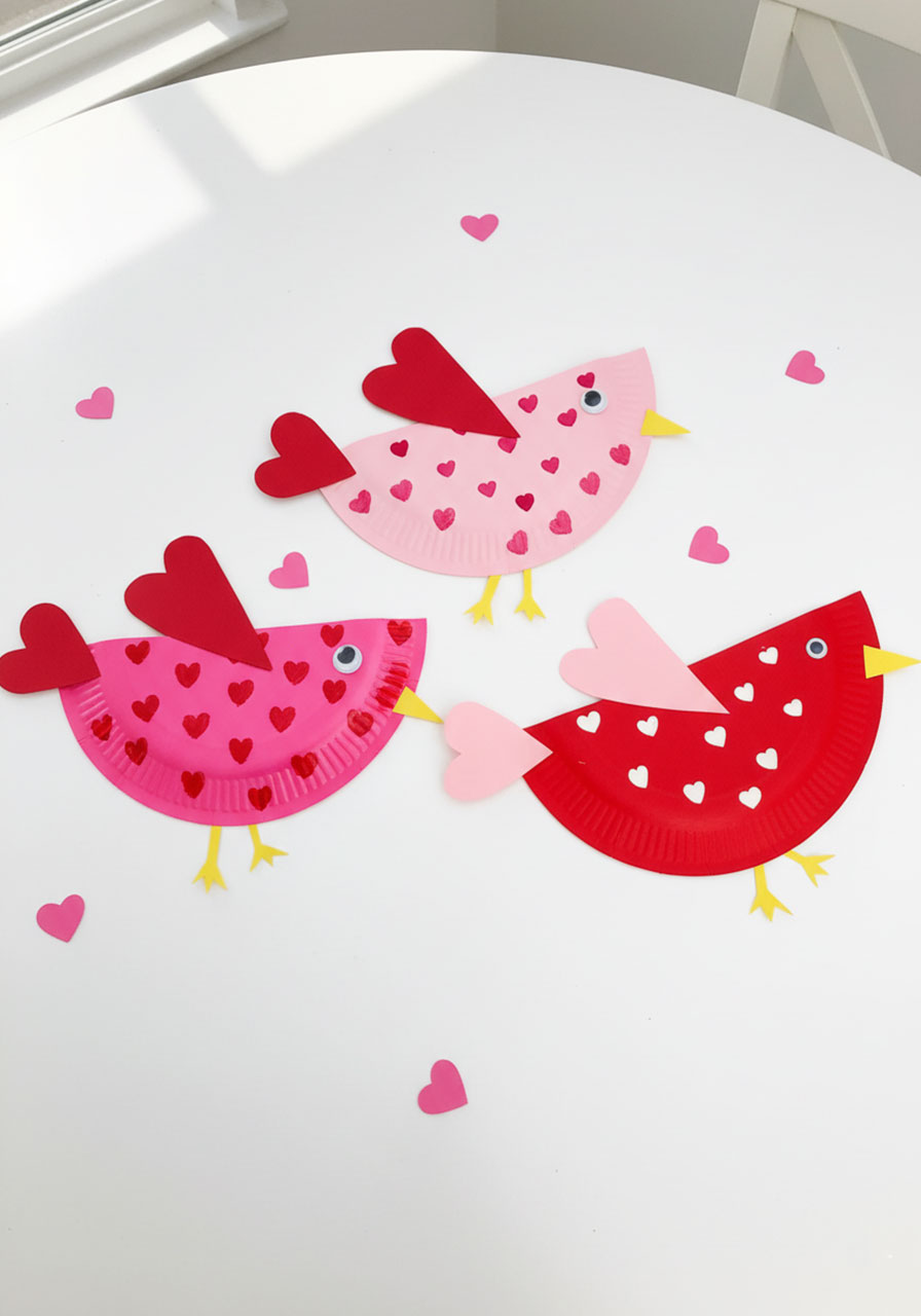 Three adorable paper plate Valentine love birds craft for kids in red and pink with heart patterns and googly eyes
