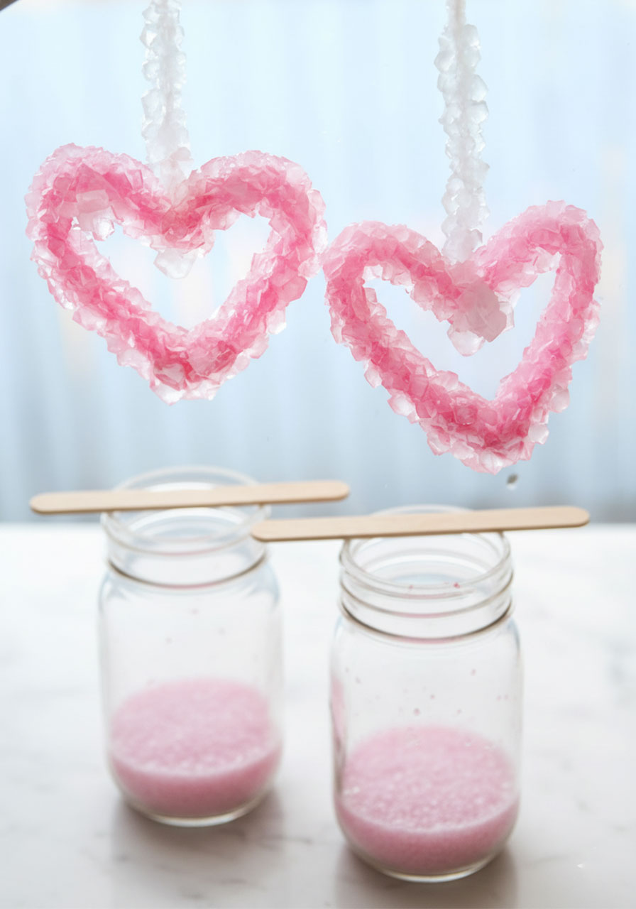 Finished pink crystal hearts made from pipe cleaners and borax hanging above mason jars showing completed Valentine's Day science experiment
