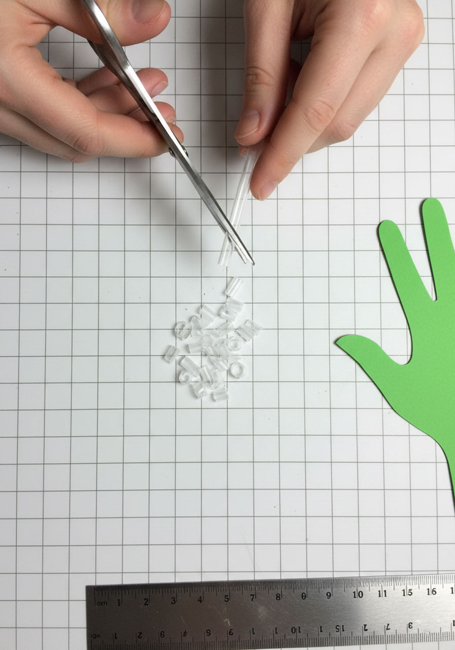 Cutting clear plastic drinking straws into small segments to represent bones for DIY robot hand STEM project