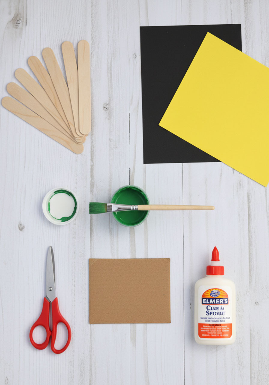 Flat lay of craft supplies needed for leprechaun hat including popsicle sticks, green paint, black and yellow paper, glue, and scissors