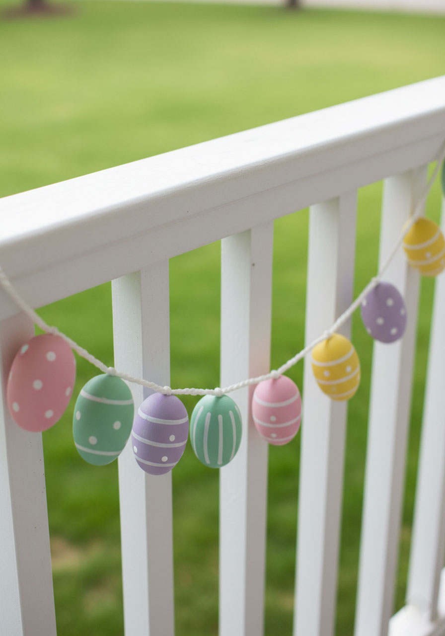 Hand-painted pastel wooden egg garland strung along a white porch railing for Easter outdoor decor
