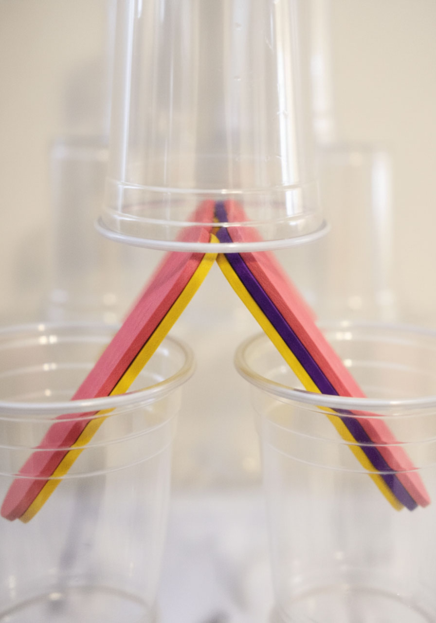 Close-up of popsicle sticks stabilizing cup connections showing building technique detail for kids tower challenge