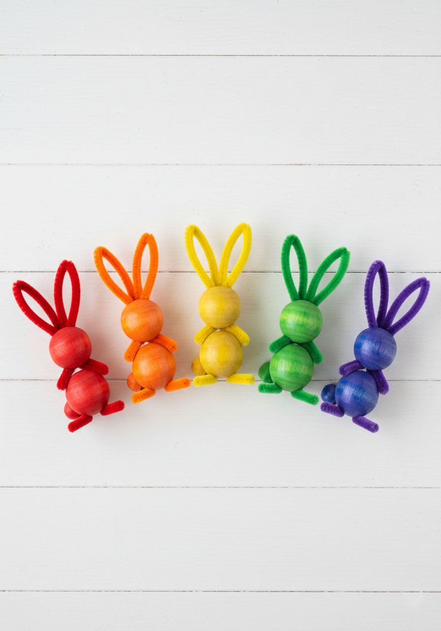Six rainbow-colored pipe cleaner bunnies with dyed wooden beads arranged in colorful arc