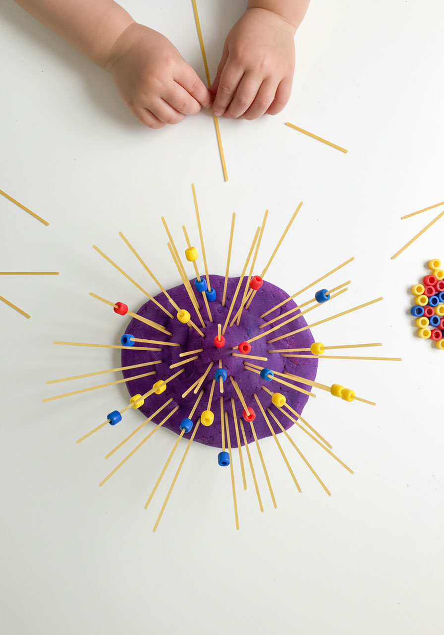 Toddler creating spaghetti playdough forest with beads to strengthen pincer grasp and fine motor skills
