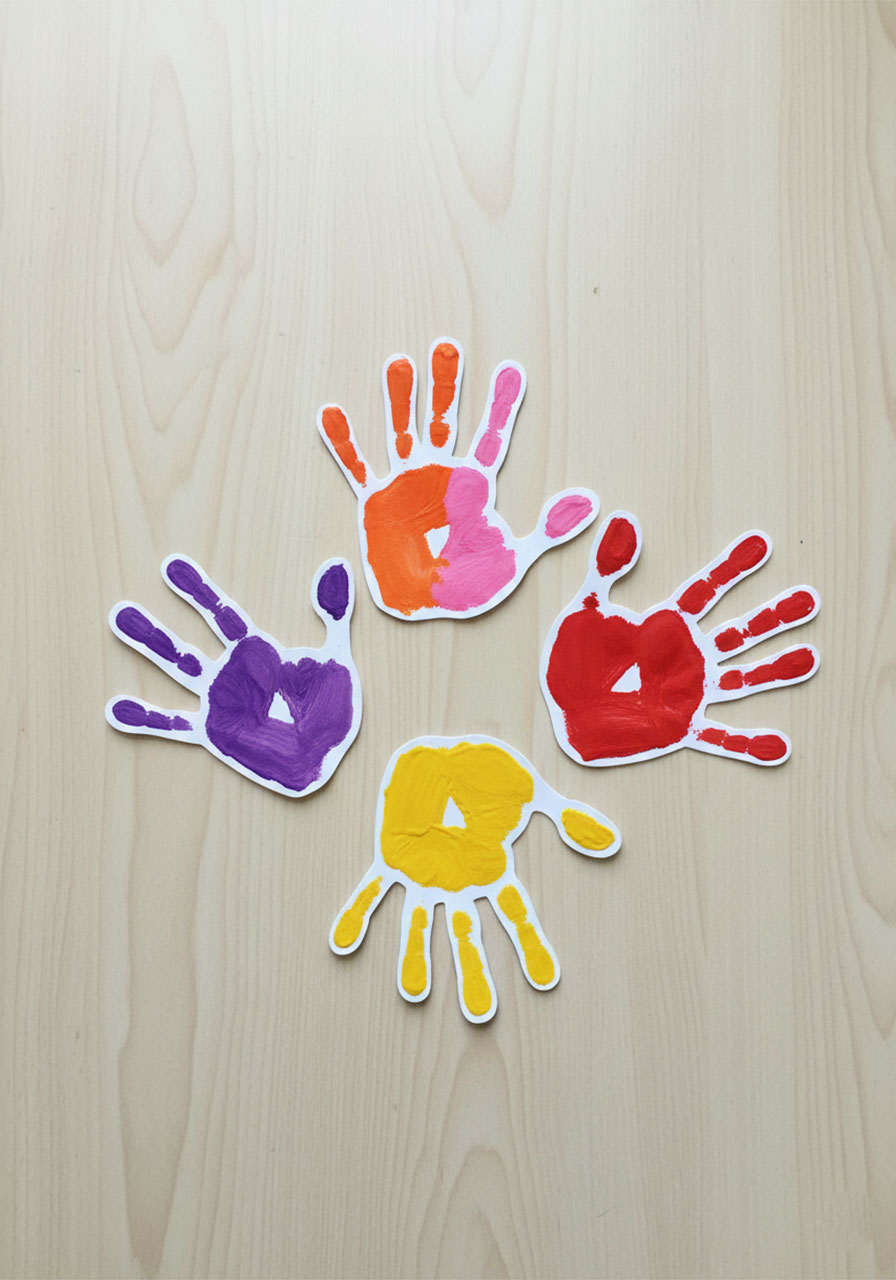 Five colorful cut-out toddler handprints in purple, pink, orange, red, and yellow laid out as flower heads for DIY Mother's Day handprint bouquet