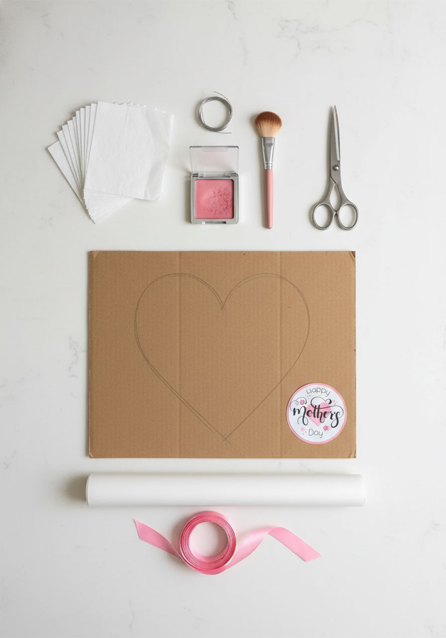 All supplies needed to make a DIY Mother's Day heart flower bouquet including tissue paper, wire, blush, scissors, and ribbon laid out on a white table
