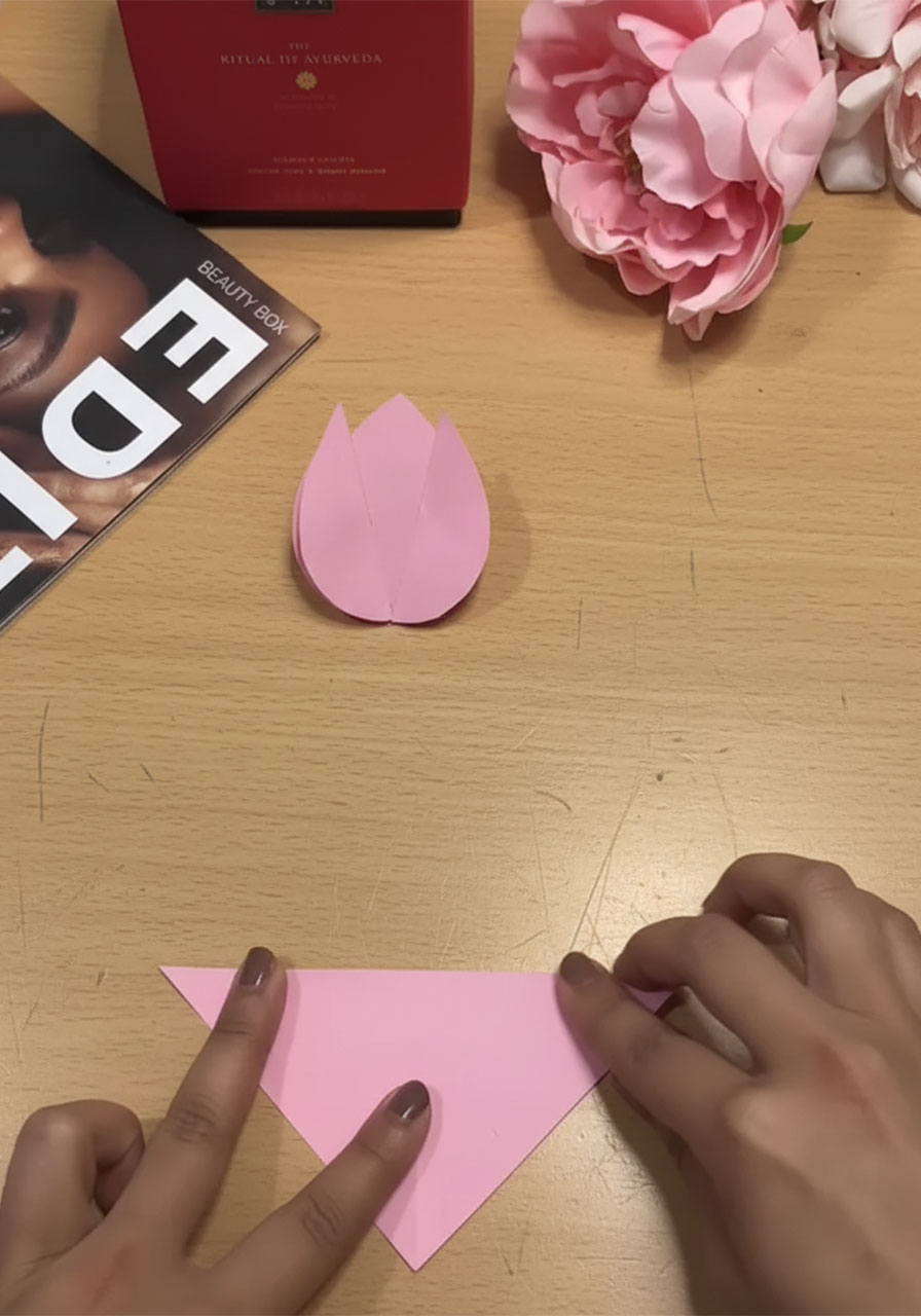 Step-by-step flat lay showing how to fold a 3D paper tulip for a DIY Mother's Day bouquet card, five stages from flat square to finished flower step1a