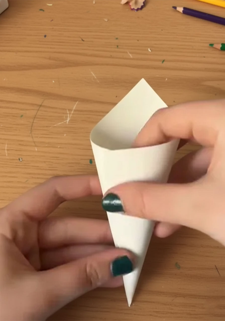 Two hands rolling white cardstock into a cone shape for a DIY paper rose bouquet, step 1 of the tutorial step1b
