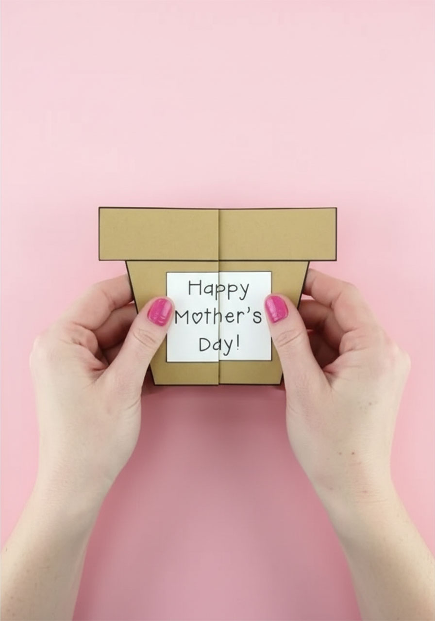 Hands folding a brown kraft cardstock flower pot shape in half to create the Mother's Day card base