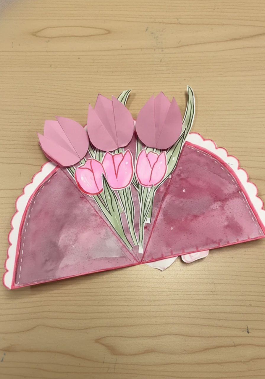 Hand lifting pink paper tulip petal on DIY Mother's Day bouquet card to reveal a hidden "Thank You" secret message underneath step3a