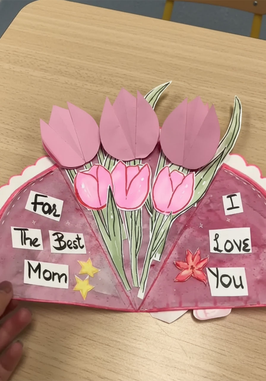 Hand lifting pink paper tulip petal on DIY Mother's Day bouquet card to reveal a hidden "Thank You" secret message underneath step3b