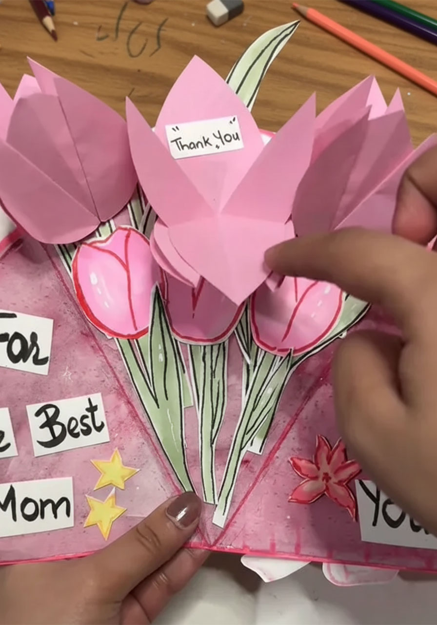 Hand lifting pink paper tulip petal on DIY Mother's Day bouquet card to reveal a hidden "Thank You" secret message underneath step3c