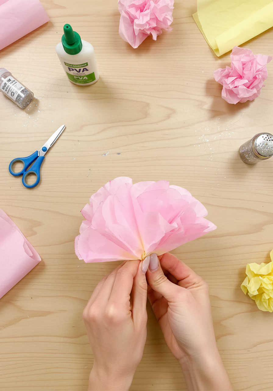 Hands shaping a pink coffee filter flower by pulling and curling each layer open into a peony shape step 5c