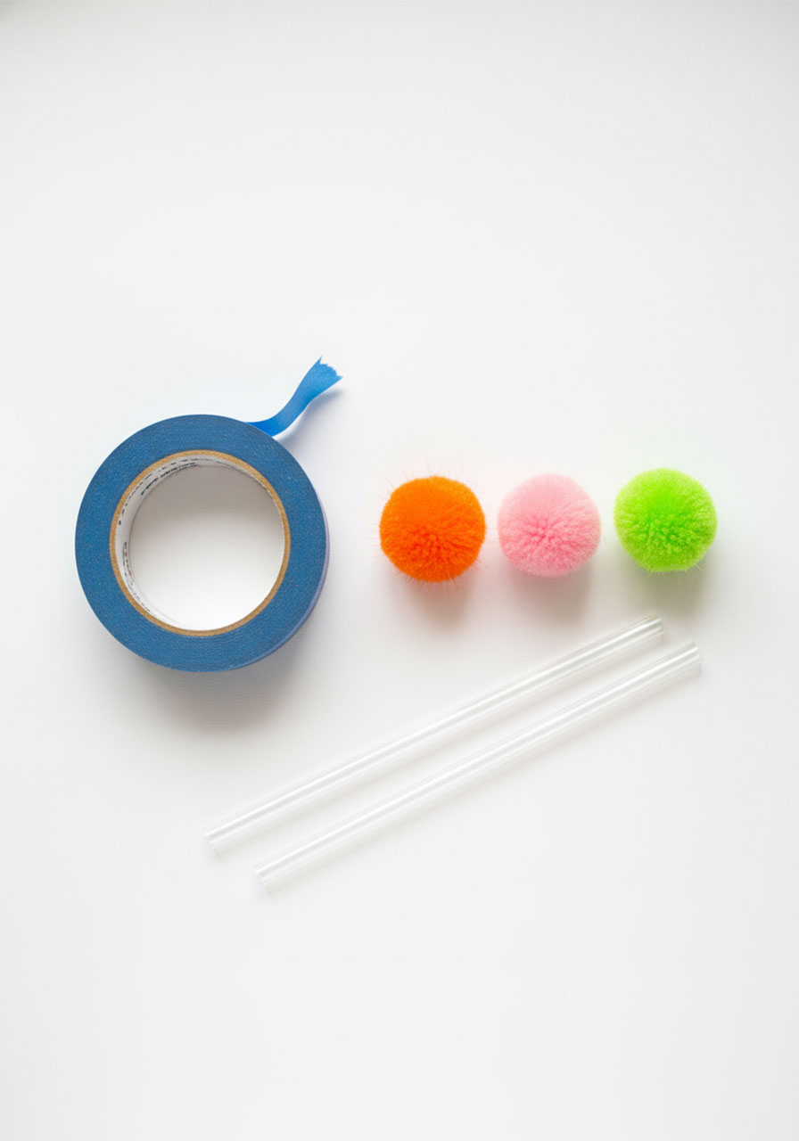 Flat lay of straw maze activity supplies including blue painter's tape, colorful pom-poms, and plastic straws