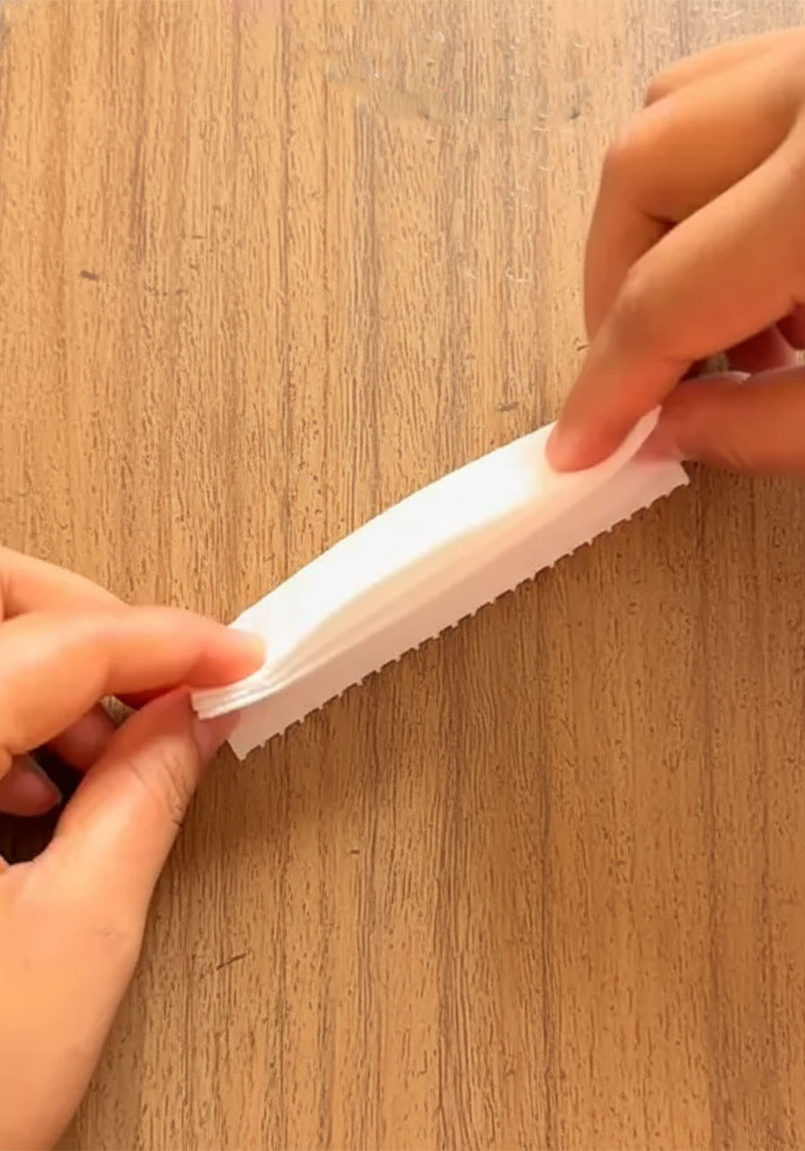 Hands accordion-folding white tissue paper squares to make a DIY tissue paper flower for a Mother's Day bouquet - 2