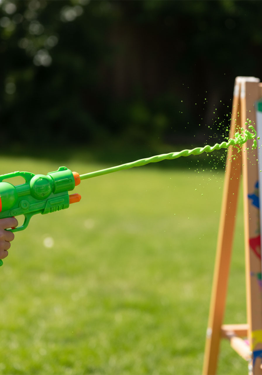 Close-up of green paint shooting from a plastic water pistol during kids water gun painting activity