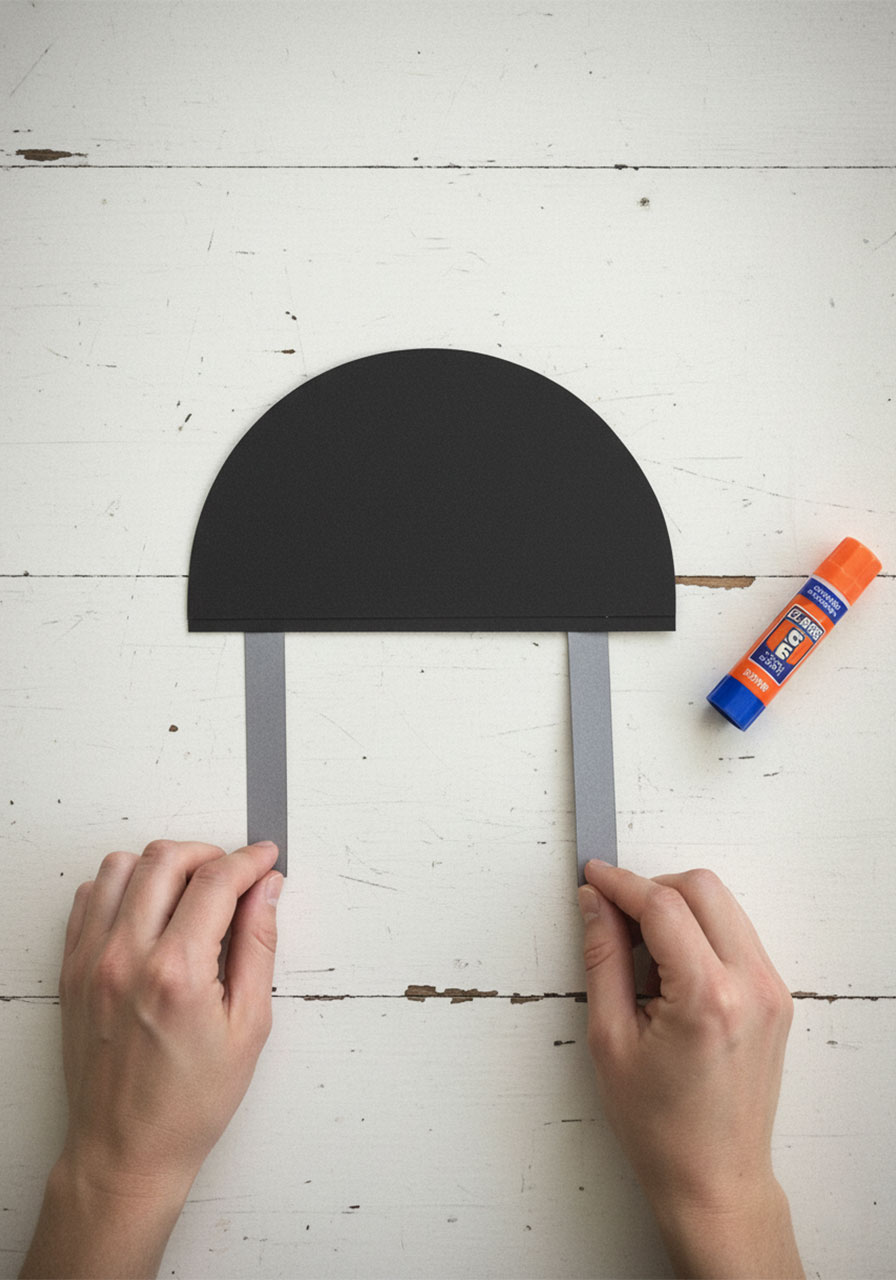 Hands pressing grey cardstock legs onto the back of a folded black grill card for a Father's Day handprint craft