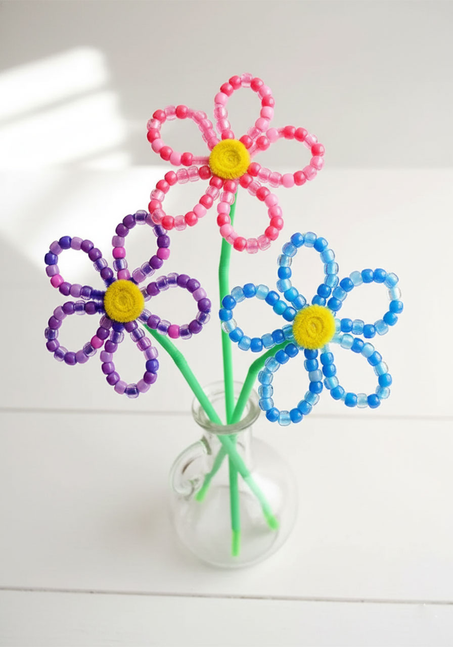 Finished beaded pipe cleaner flowers bouquet in pink, blue, and purple displayed in a clear glass vase — easy summer kids craft