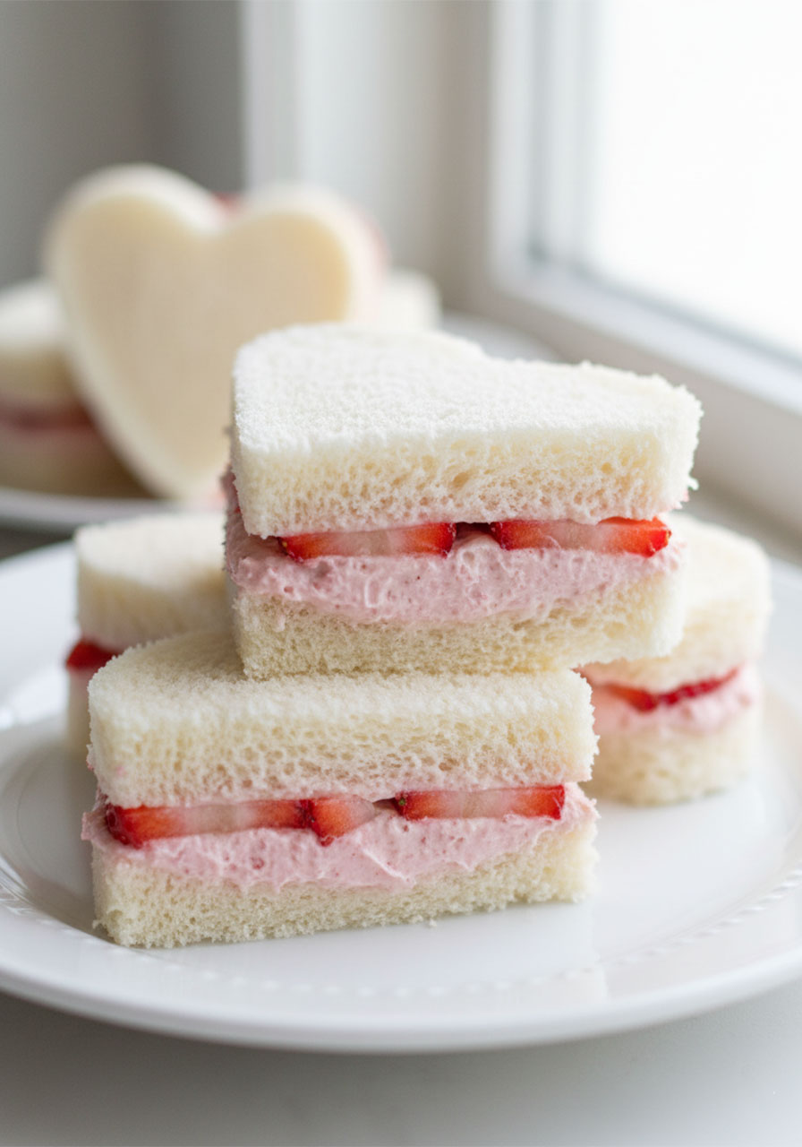Close-up of a closed heart-shaped strawberry tea sandwich showing the cream cheese and fresh strawberry filling layers