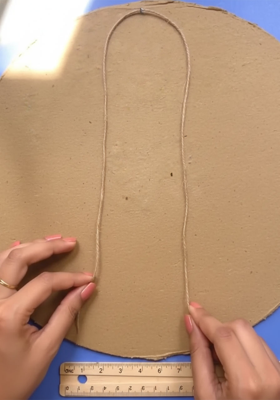 Hands shaping jute twine into an inverted U-shaped hanger loop for Father's Day popsicle stick wall hanging craft