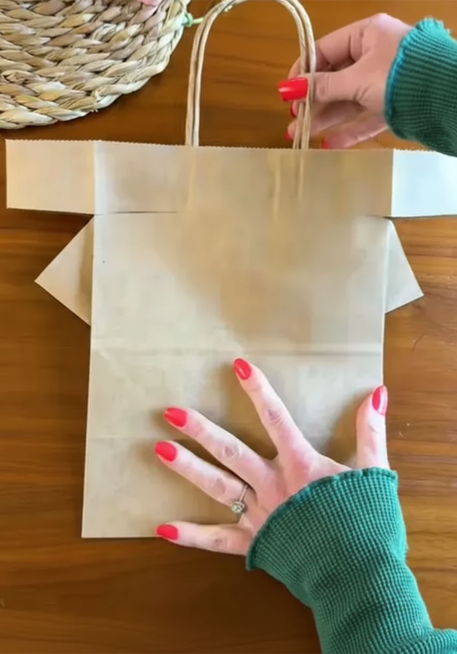 Hands folding the top corners of a brown paper bag inward to create a shirt collar shape for a DIY Father's Day gift wrap step2c