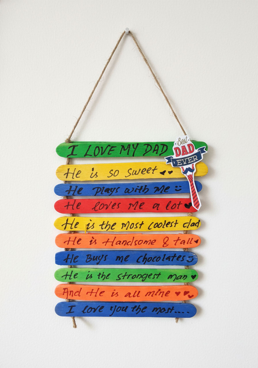Finished Father's Day popsicle stick wall hanging with rainbow colored sticks and handwritten love messages on jute twine hanger