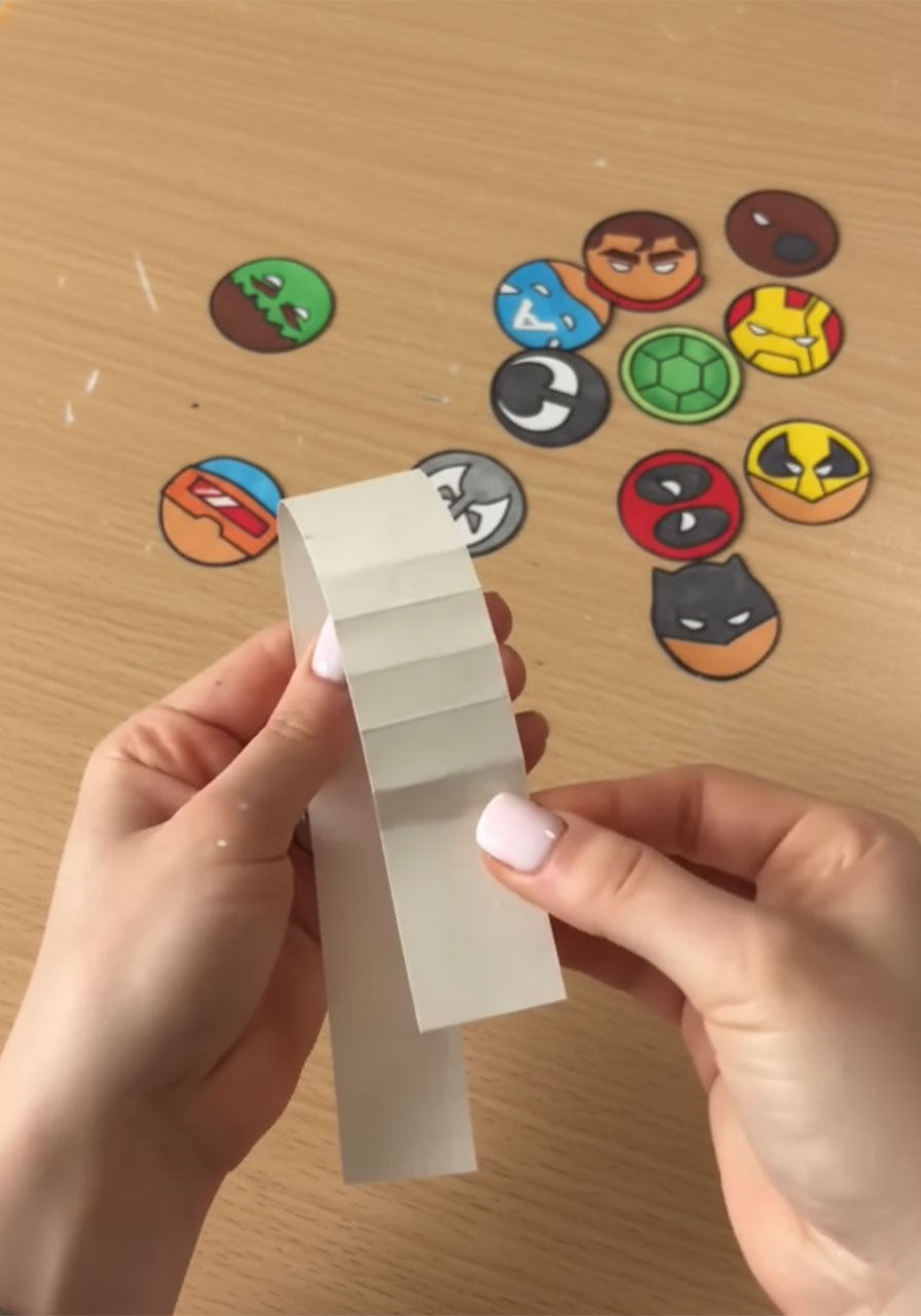 Folding white cardstock into an accordion strip for the DIY superhero pop-up card paper mechanism	phase 2 step4b