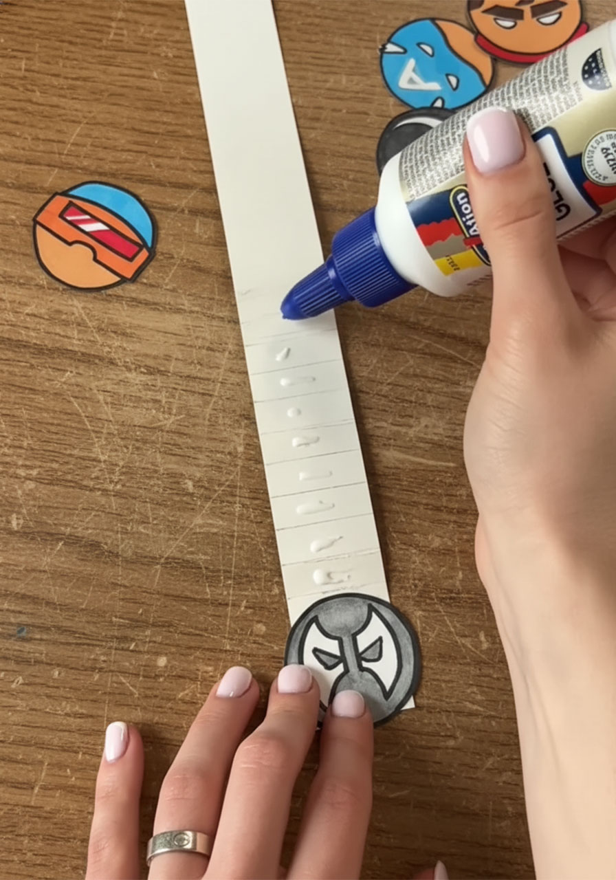 Gluing colorful superhero circle cutouts onto each fold of the accordion strip for a DIY Father's Day pop-up card phase 2 step6b