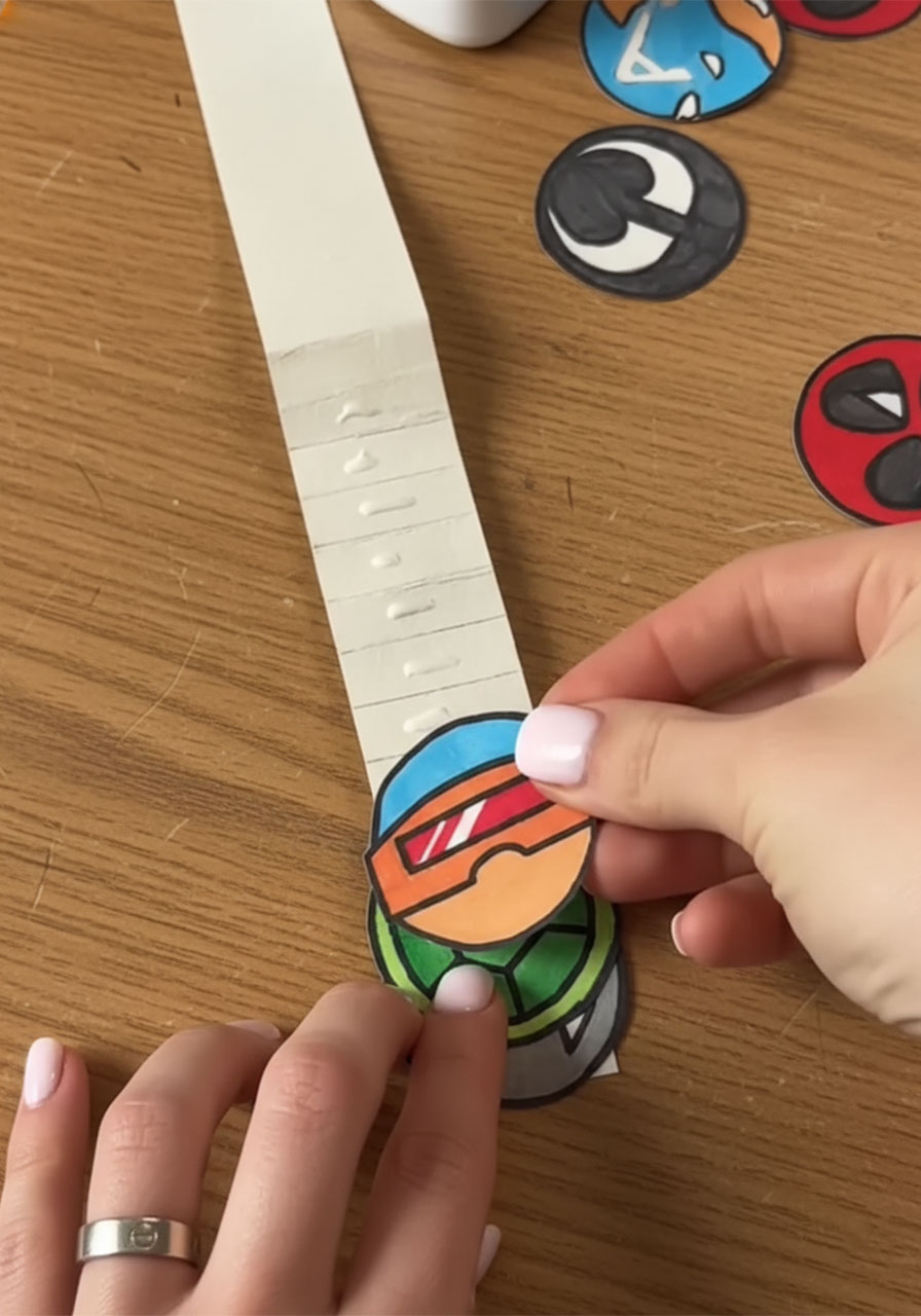Gluing colorful superhero circle cutouts onto each fold of the accordion strip for a DIY Father's Day pop-up card phase 2 step6c