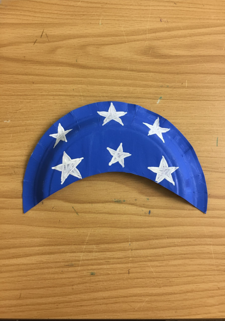 Blue painted paper plate crescent with seven hand-painted white stars for patriotic Fourth of July paper plate hat craft