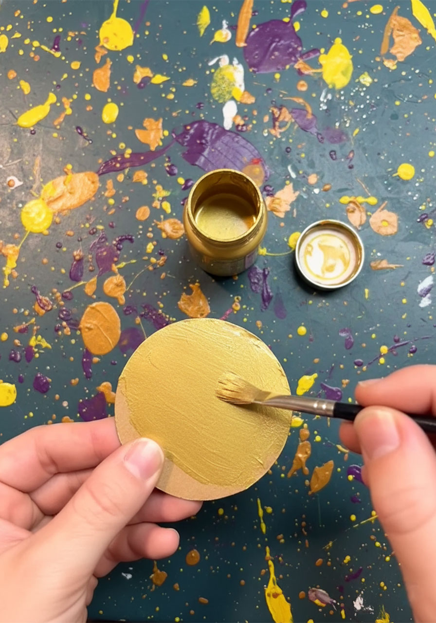 Child painting a cardboard circle gold with metallic craft paint as part of a DIY Father's Day award ribbon craft, Step 2