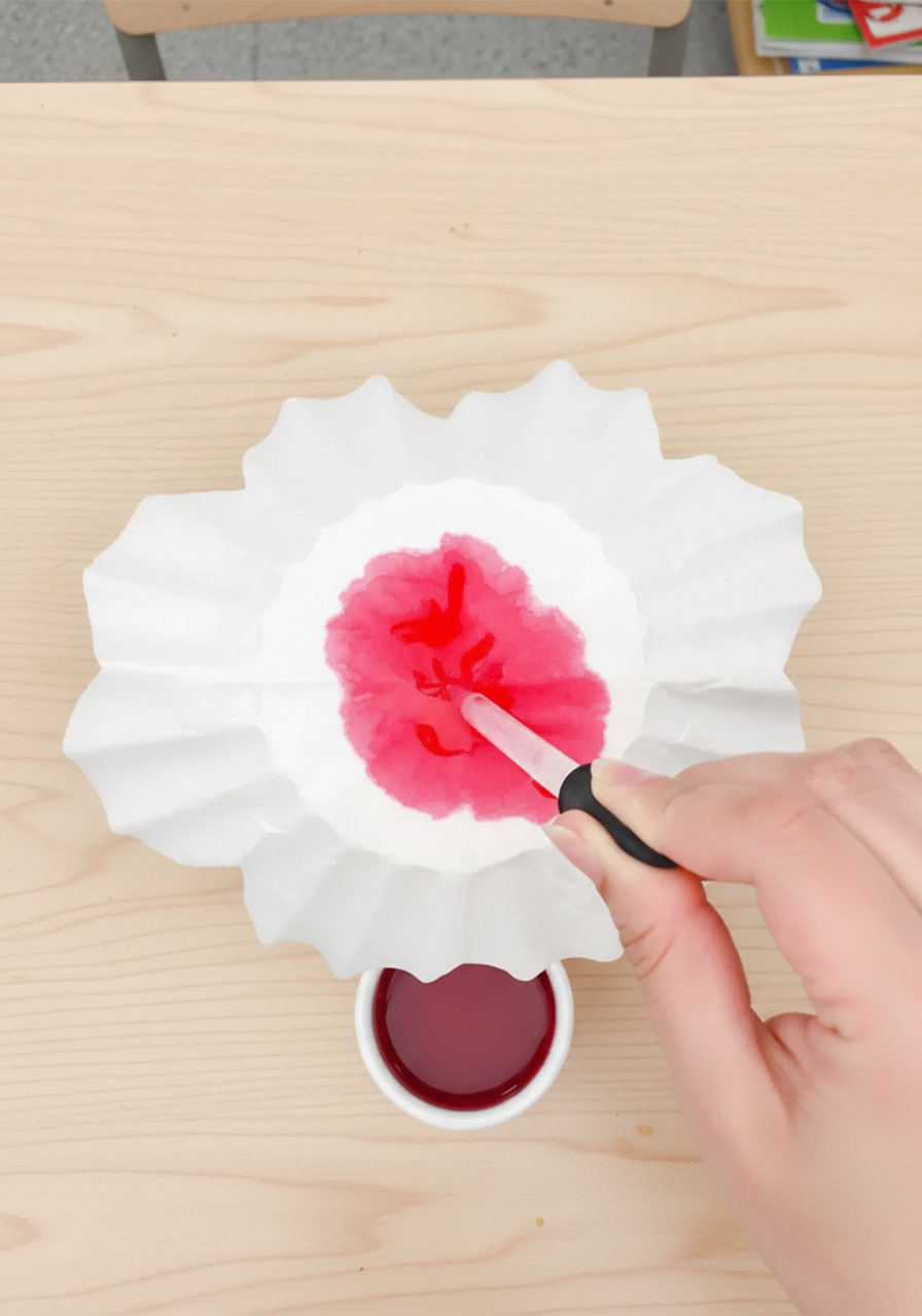Applying red liquid watercolor paint to coffee filters draped over a glass to create beautiful ombre blush pink rose petals step3c