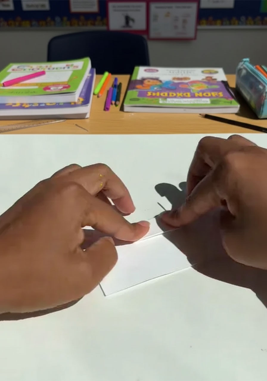 Adult hands cutting two parallel slits into folded white cardstock to create a pop-up tab mechanism step 1d
