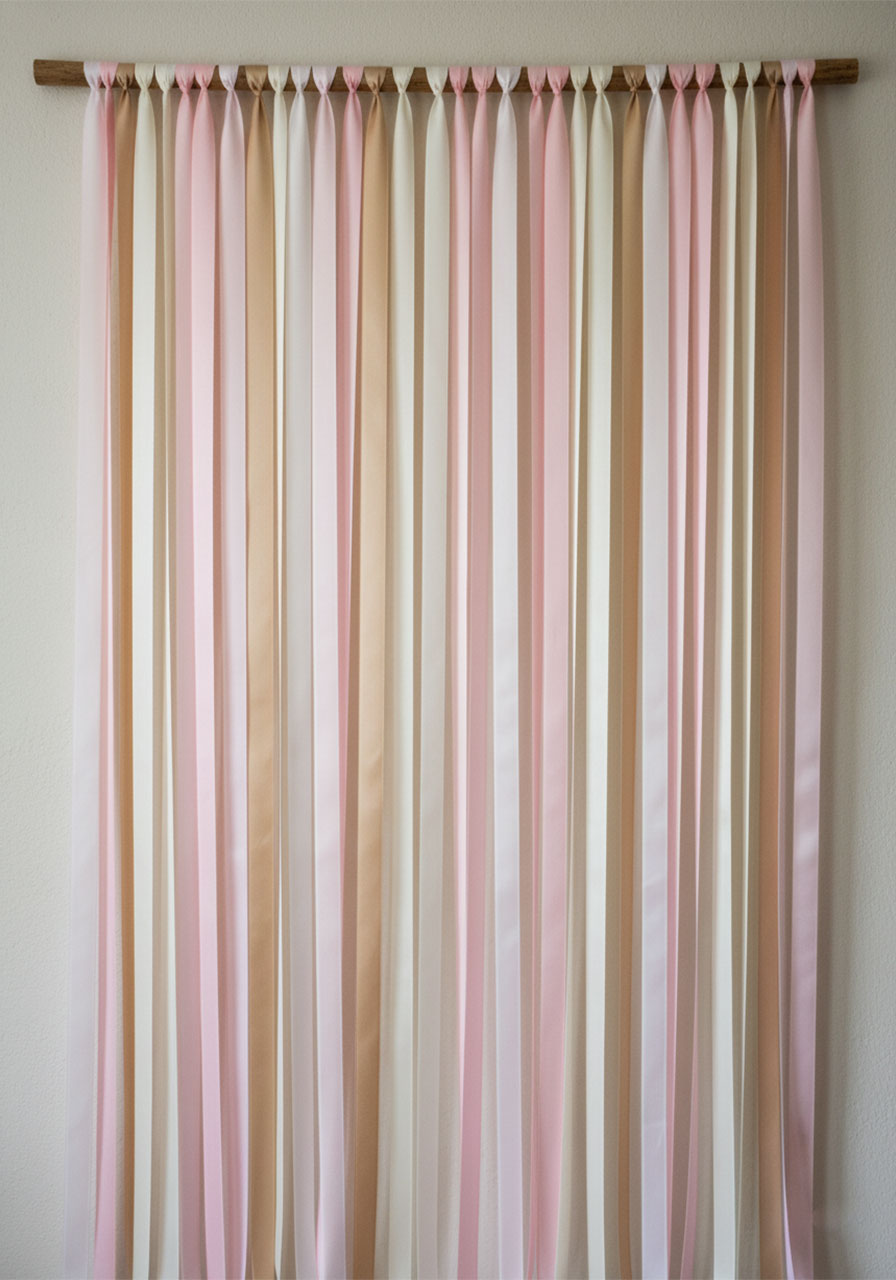 Elegant satin ribbon garland backdrop in blush and cream for a tea party photo wall.