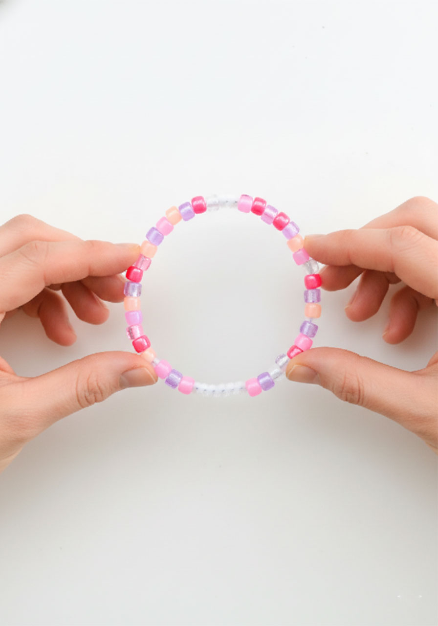 Hands twisting the bare wire ends of a fully beaded pipe cleaner together to form a circular ring shape for butterfly wings step2b