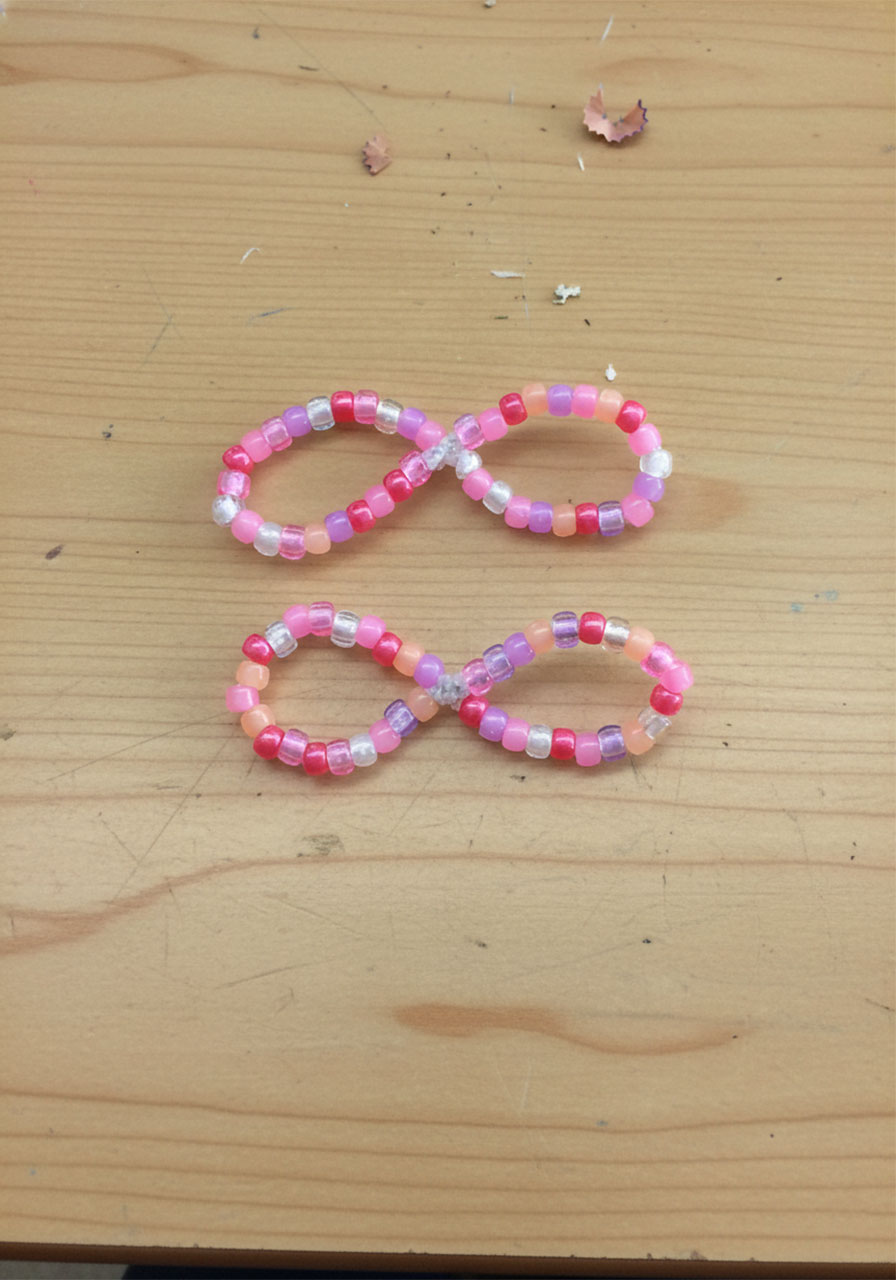 Two hands pinching a beaded pipe cleaner circle at top and bottom simultaneously to form a figure-eight shape representing two butterfly wings step3a