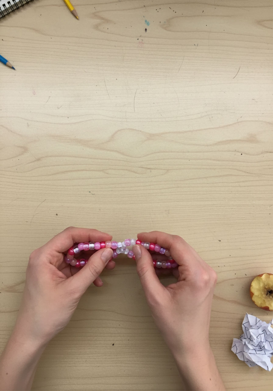 Thumbs spreading pony beads apart at the top and bottom of a beaded pipe cleaner circle to reveal bare wire for pinching into butterfly wing shape