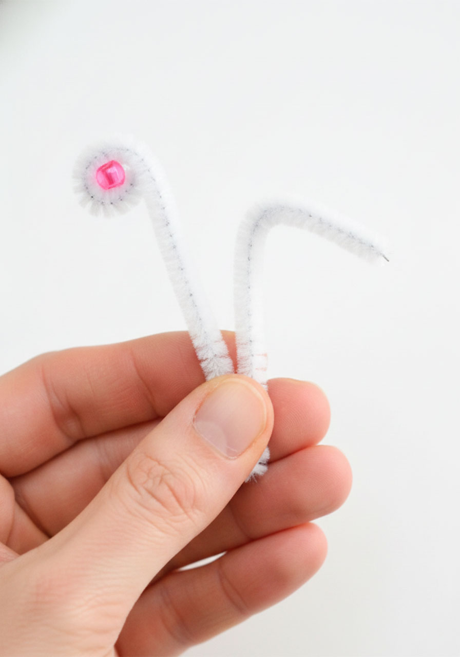 Hand holding a folded pipe cleaner showing one end curled into a spiral with a pink pony bead tip and one straight end for butterfly antennae comparison