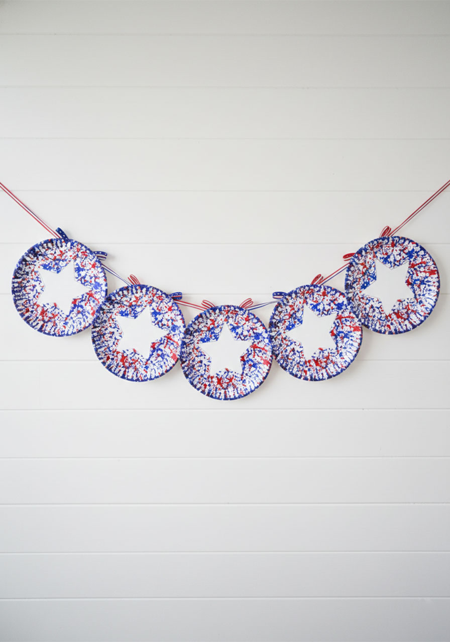 Five straw stamped paper plate 4th of July crafts linked as a patriotic garland hung on white wall as festive holiday home decoration