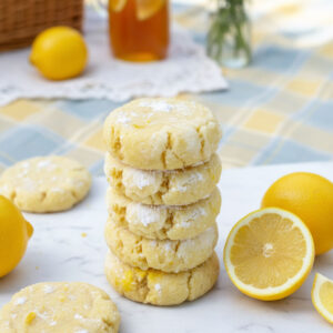 Stack of sugar free lemon cookies dusted with powdered sweetener on white marble surface with fresh lemon