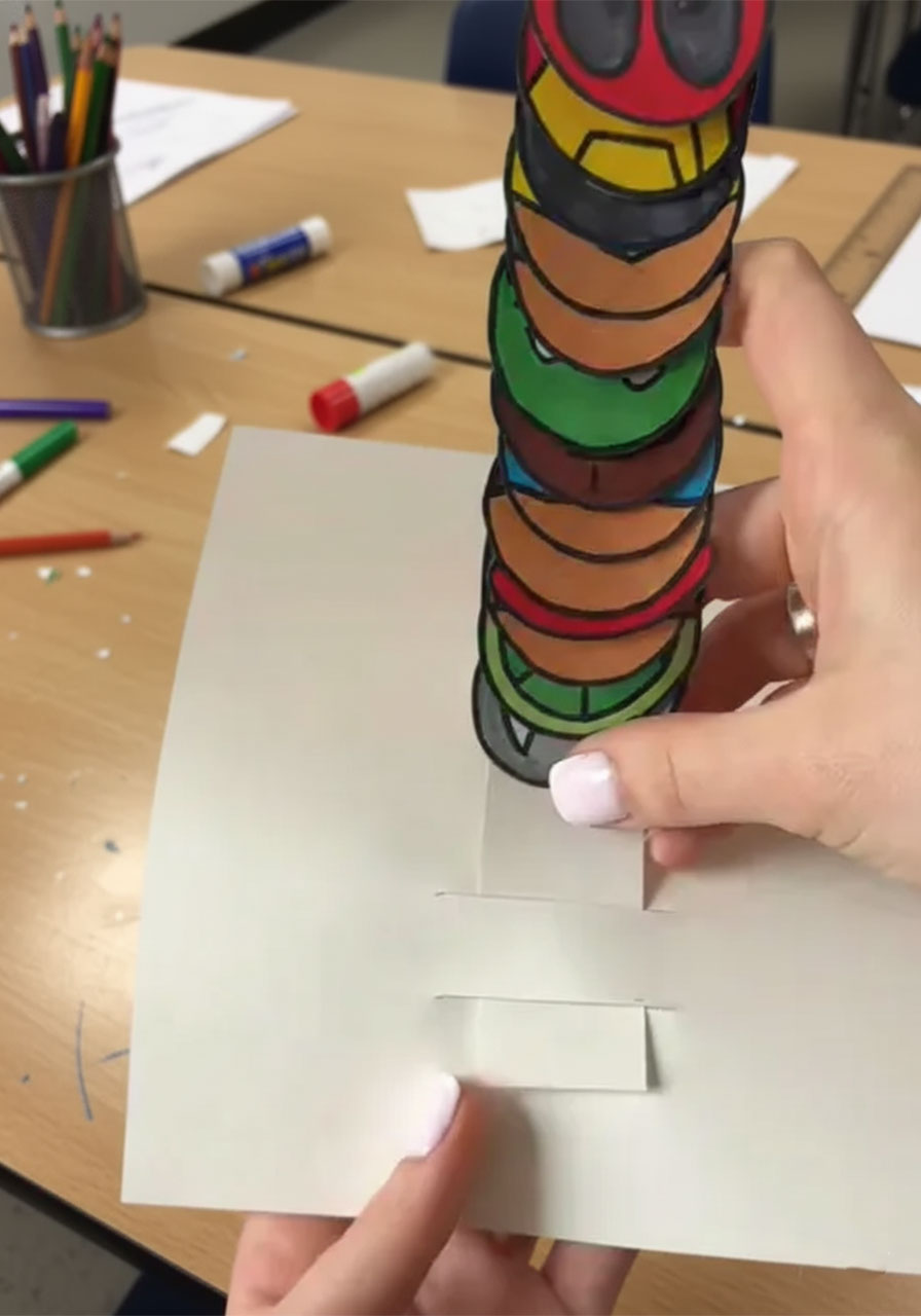 Threading the superhero accordion strip through the card slits during DIY pop-up Father's Day card assembly	phase 3 step 3